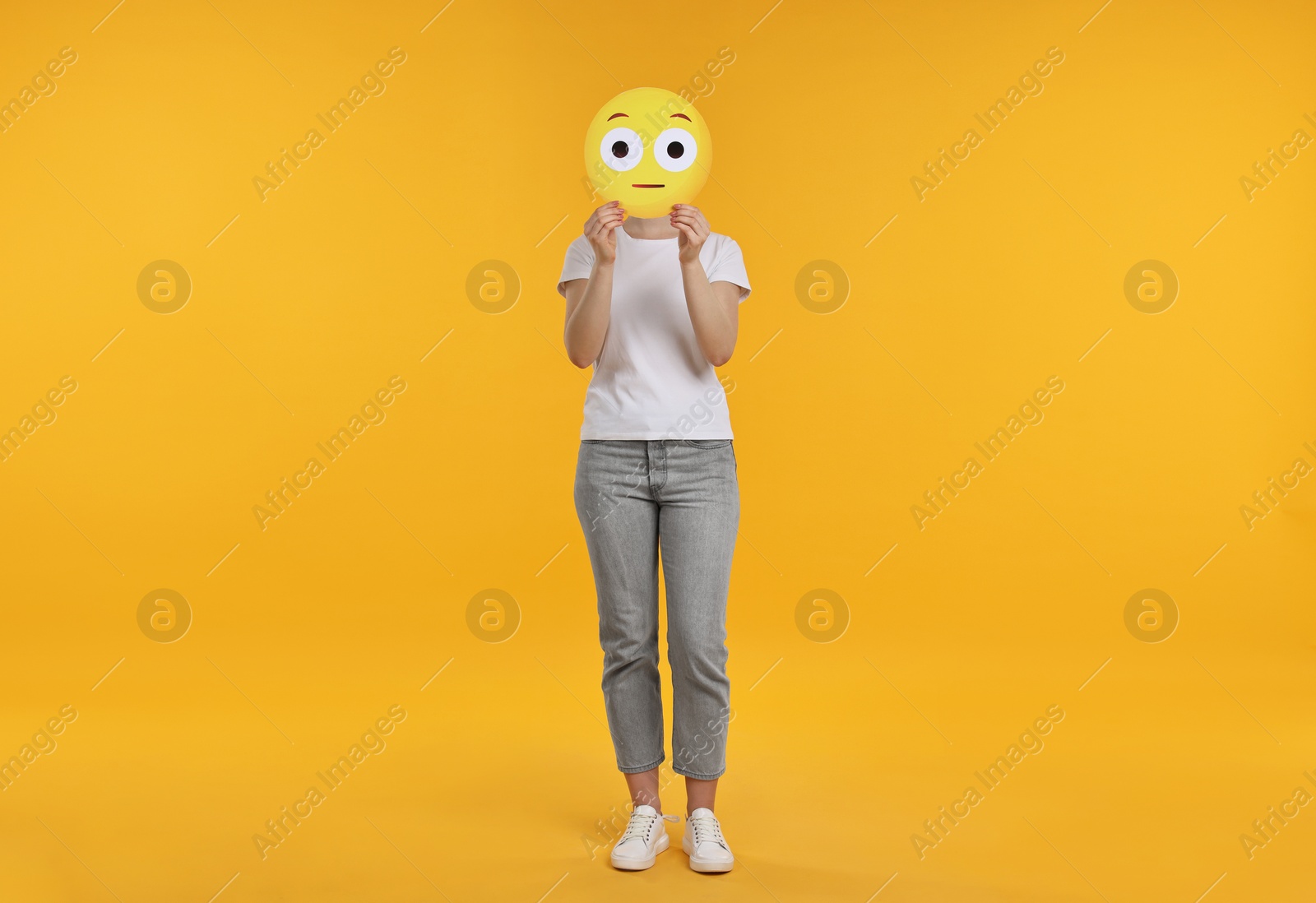 Photo of Woman covering face with surprised emoticon on yellow background