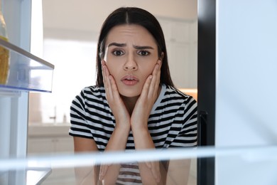 Upset woman near empty refrigerator in kitchen, view from inside