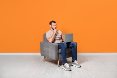 Photo of Young man using laptop while sitting in armchair indoors