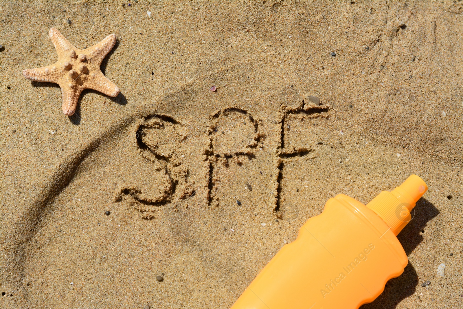 Photo of Abbreviation SPF written on sand, blank bottle of sunscreen and starfish at beach, flat lay