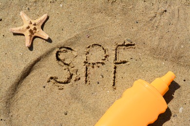 Abbreviation SPF written on sand, blank bottle of sunscreen and starfish at beach, flat lay