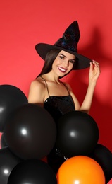 Photo of Beautiful young woman wearing witch costume with balloons for Halloween party on red background