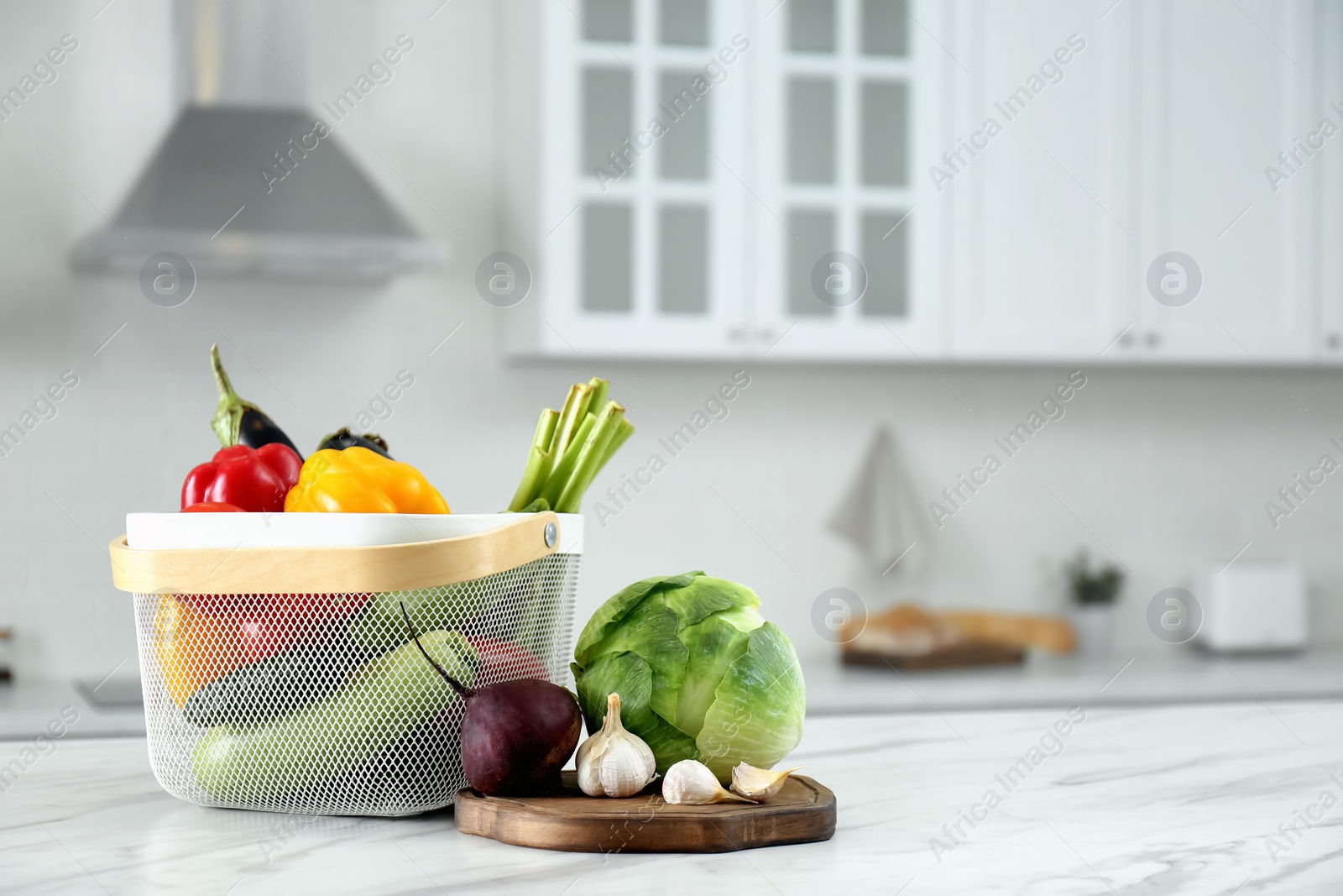 Photo of Different fresh vegetables in basket on white kitchen table. Space for text