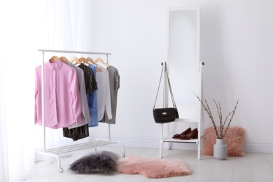 Photo of Rack with clothes and modern mirror in light room