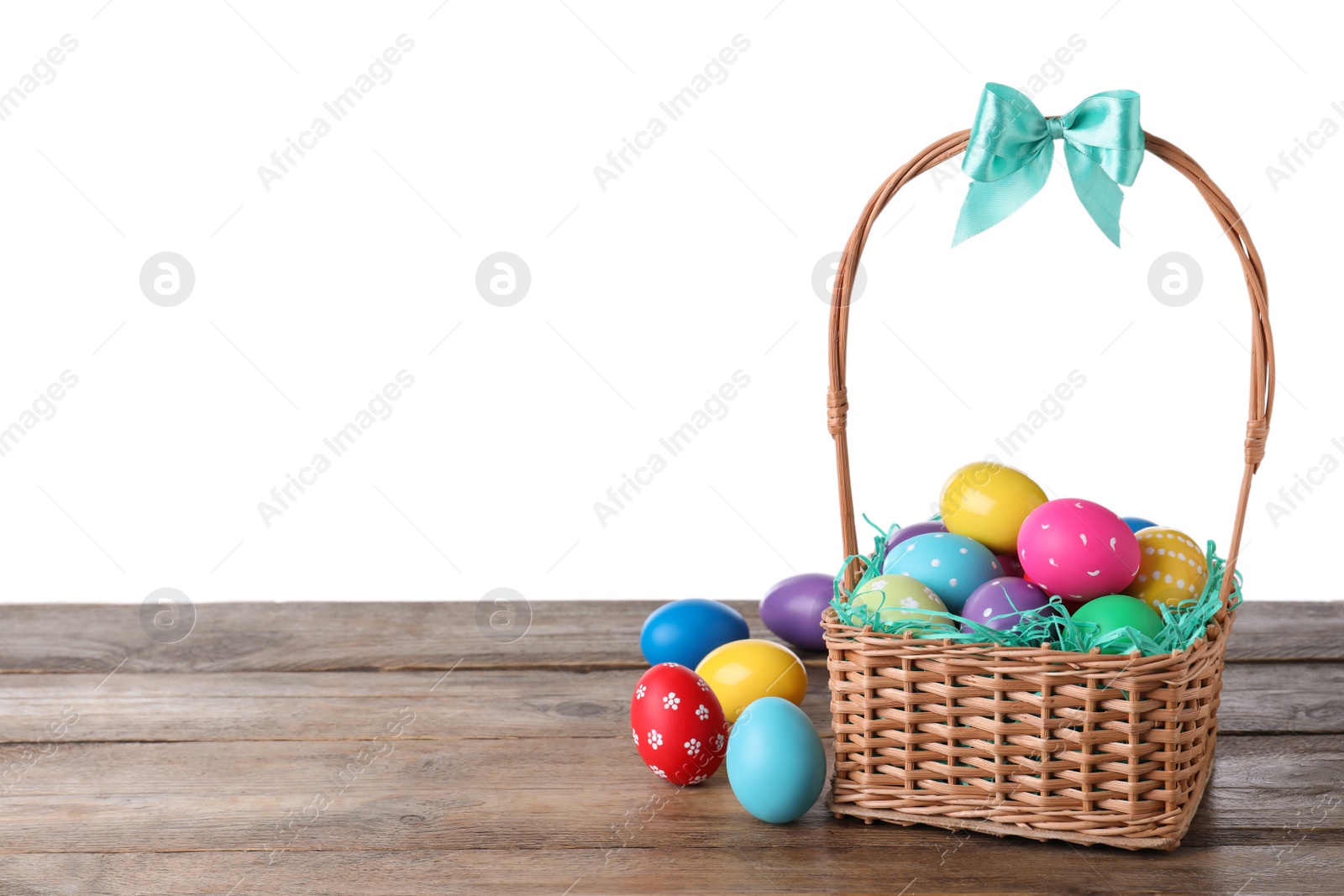 Photo of Colorful Easter eggs in wicker basket on wooden table against white background