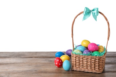 Colorful Easter eggs in wicker basket on wooden table against white background