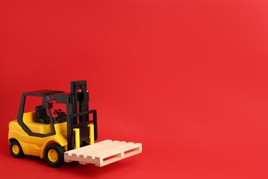 Photo of Toy forklift with wooden pallet on red background, space for text