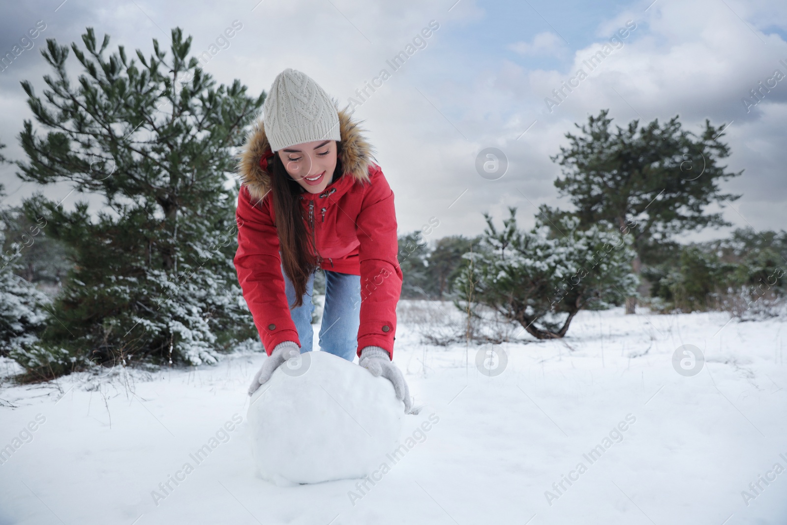 Photo of Young woman rolling snowball outdoors on winter day. Space for text