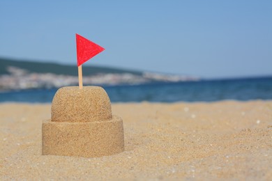 Photo of Beautiful sand castle with red flag on beach near sea, space for text