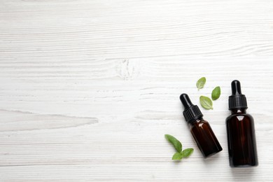 Photo of Glass bottles of basil essential oil and leaves on white  wooden table, flat lay. Space for text