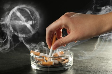 No Smoking, round sign with crossed cigarette of smoke. Woman extinguishing cigarette in glass ashtray
at grey table against black background, closeup