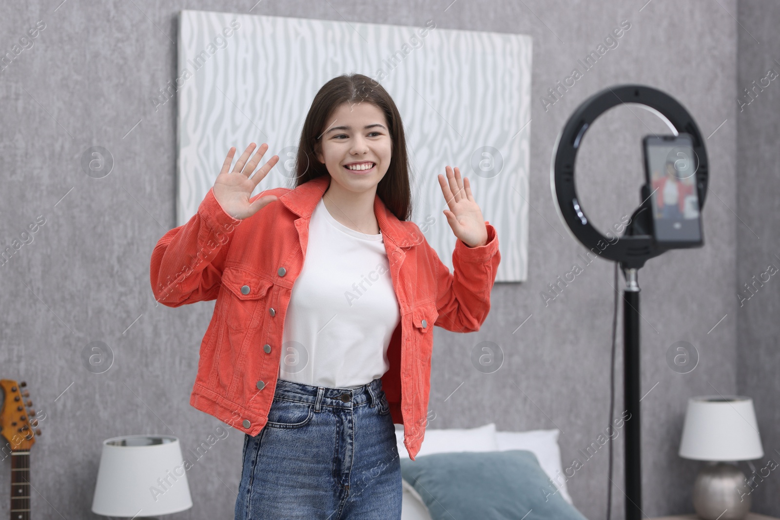 Photo of Smiling teenage blogger waving hello to her subscribers while streaming at home