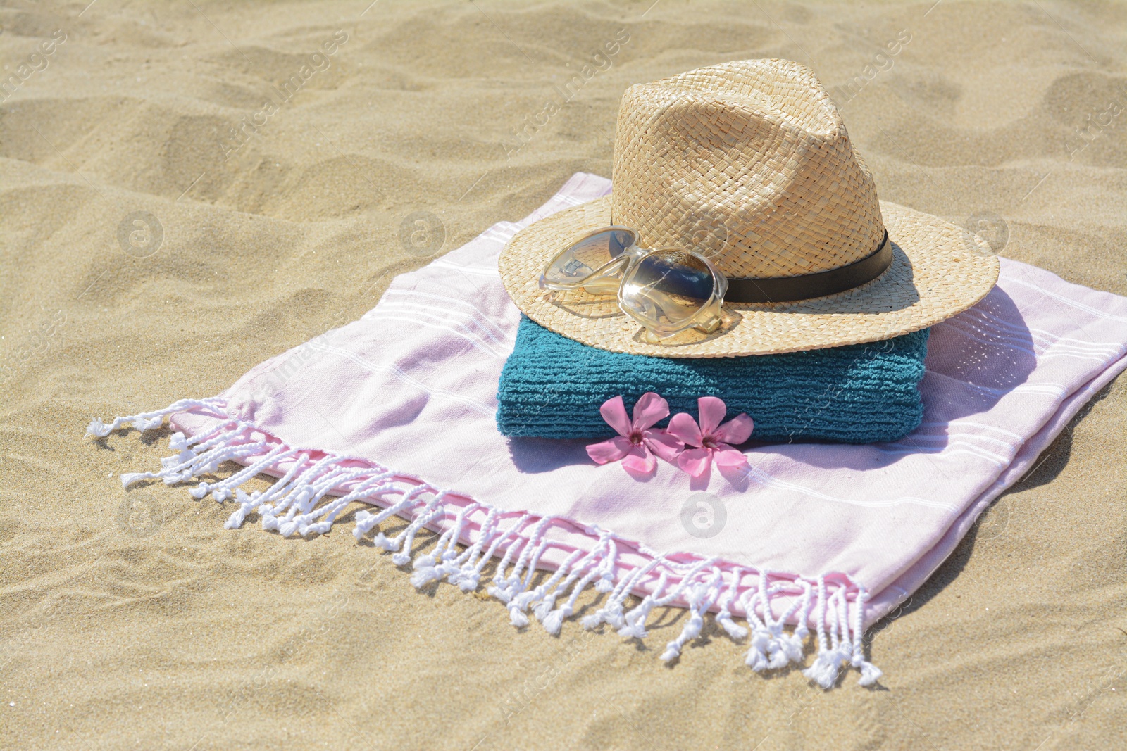 Photo of Stylish beach accessories and flowers on sand outdoors