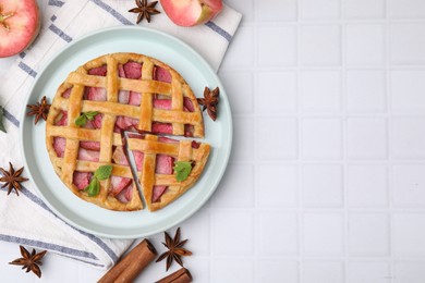 Photo of Delicious apple pie with mint and ingredients on white tiled table, flat lay. Space for text