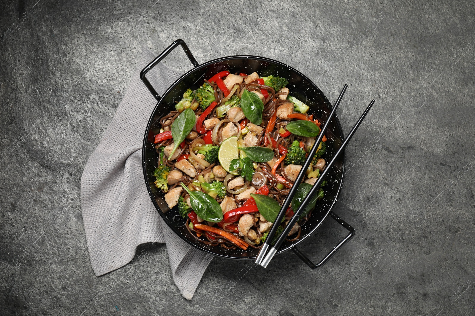 Photo of Stir-fry. Tasty noodles with meat in wok and chopsticks on grey textured table, top view