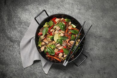 Stir-fry. Tasty noodles with meat in wok and chopsticks on grey textured table, top view