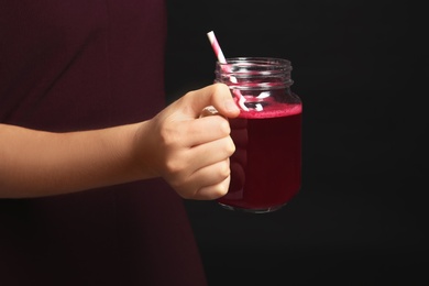 Woman with mason jar of beet smoothie on black background, closeup