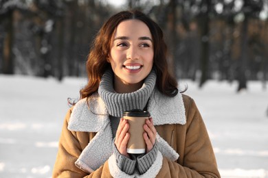 Photo of Portrait of smiling woman with paper cup of coffee in snowy park