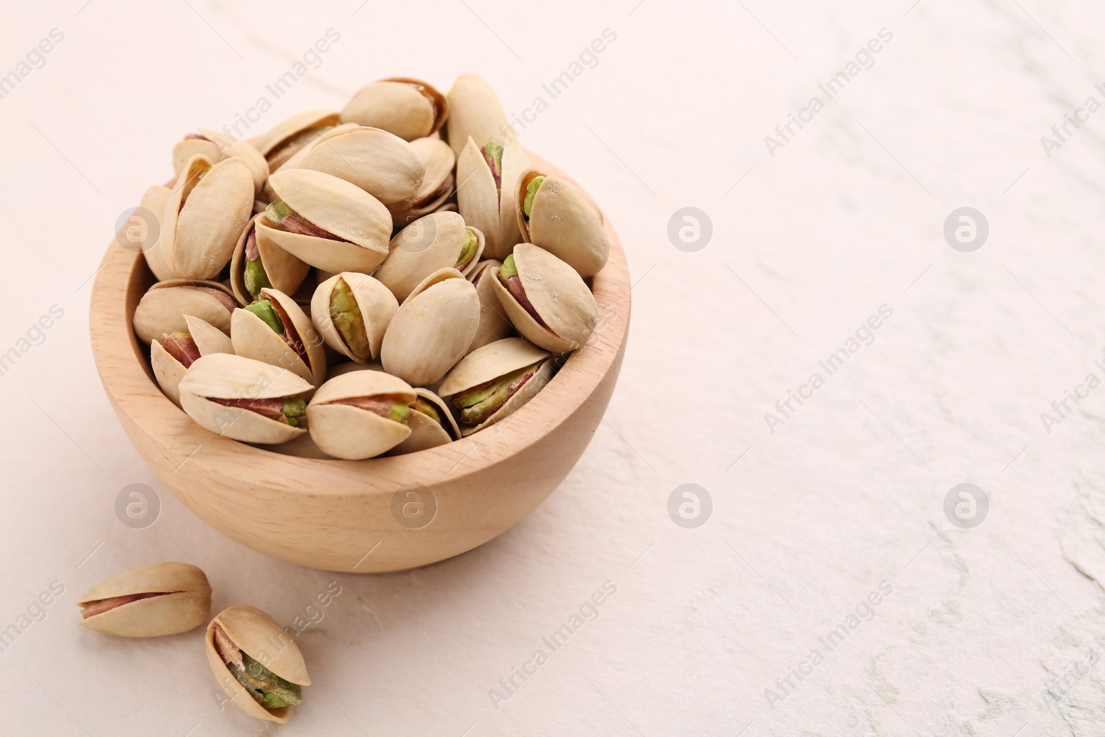 Photo of Delicious pistachios in bowl on white textured table. Space for text