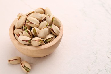 Photo of Delicious pistachios in bowl on white textured table. Space for text