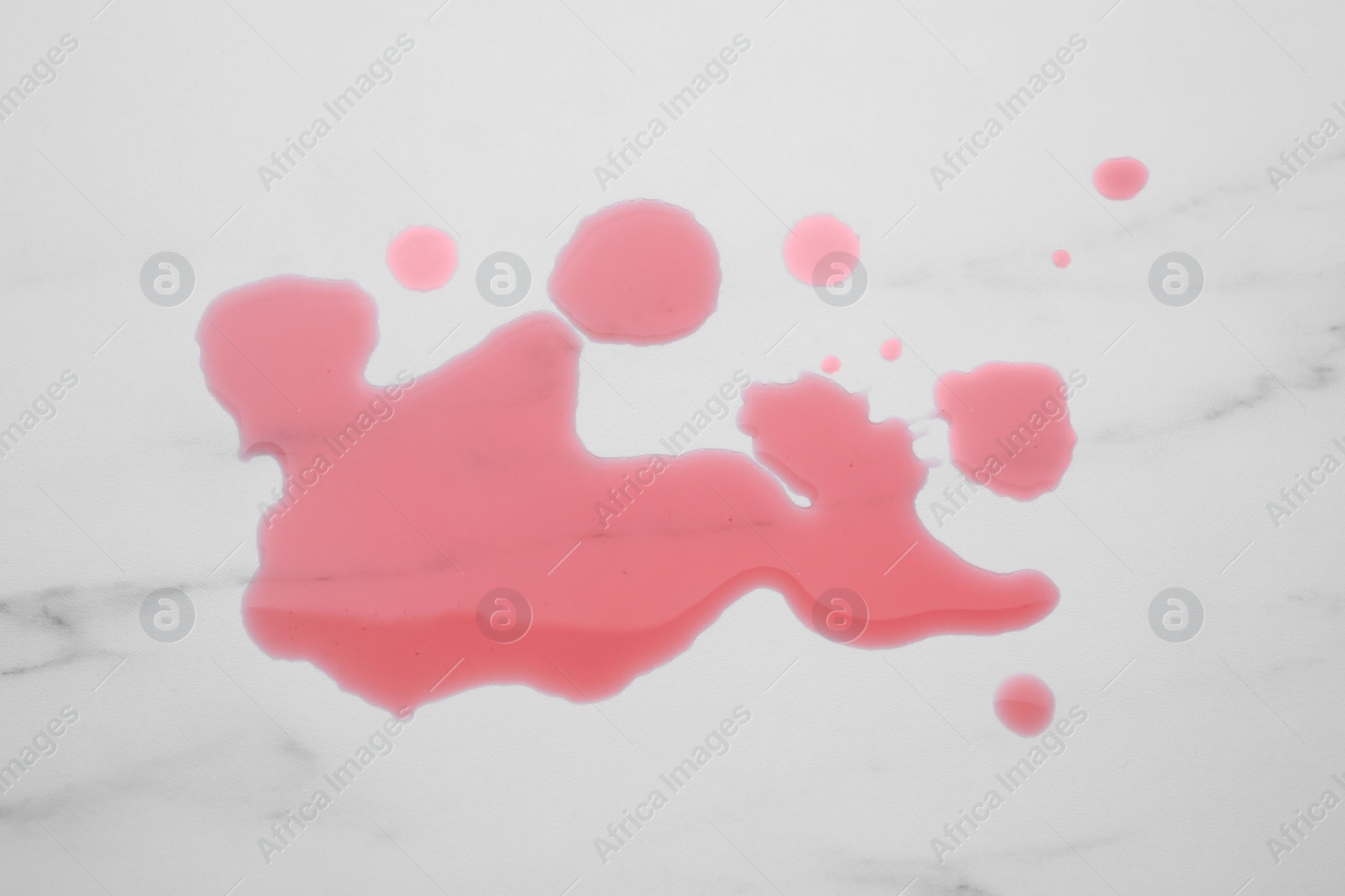 Photo of Puddle of red liquid on white marble surface, top view