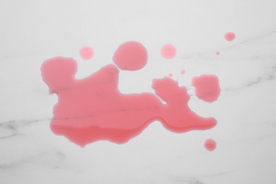 Photo of Puddle of red liquid on white marble surface, top view