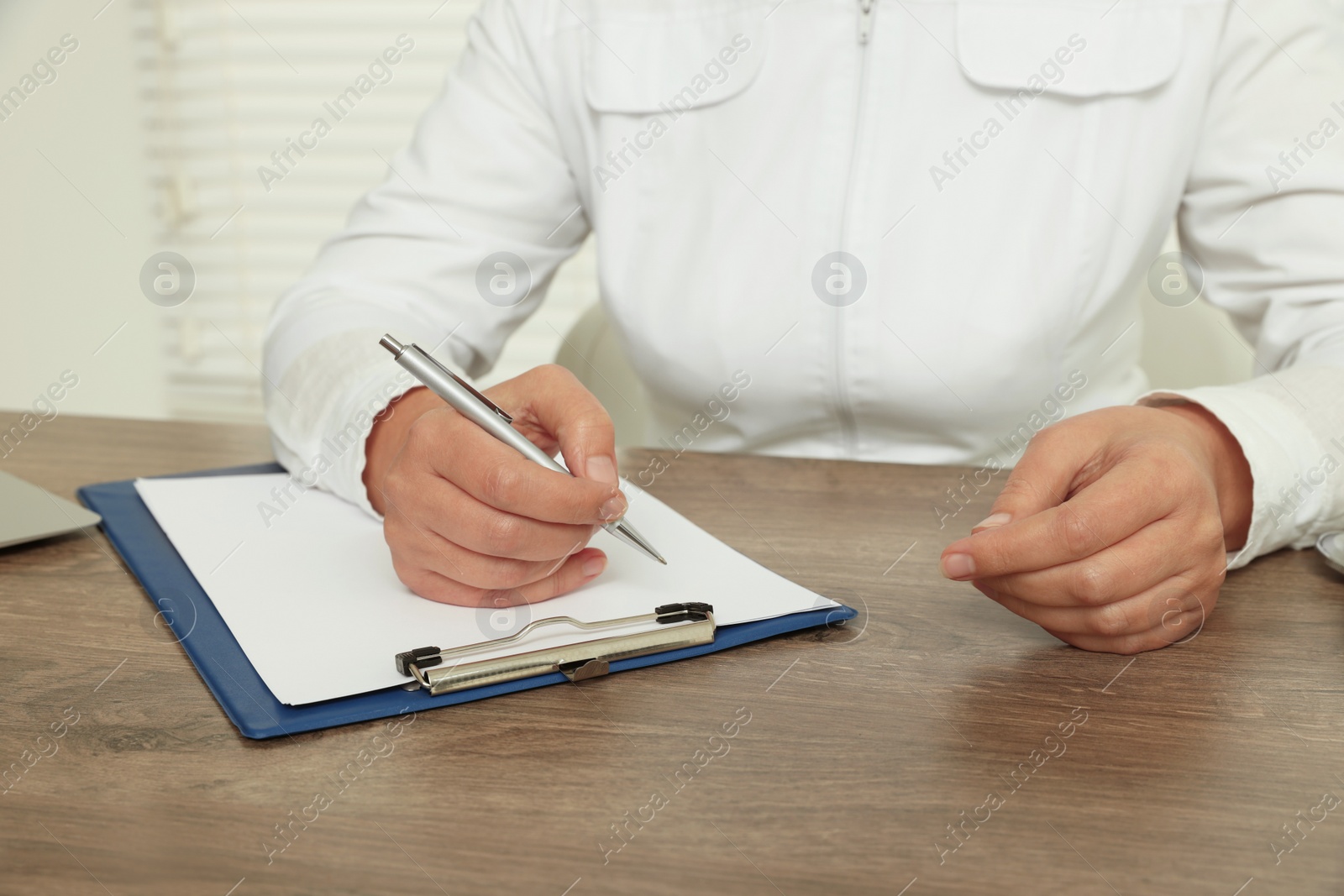 Photo of Professional doctor writing in clipboard at wooden table, closeup