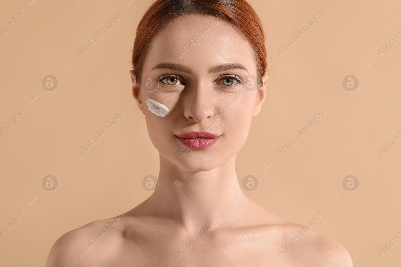 Photo of Beautiful young woman with sun protection cream on her face against beige background