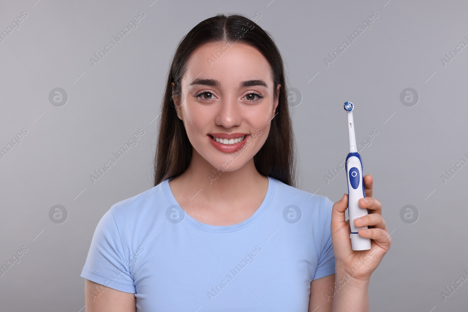 Photo of Happy young woman holding electric toothbrush on light grey background