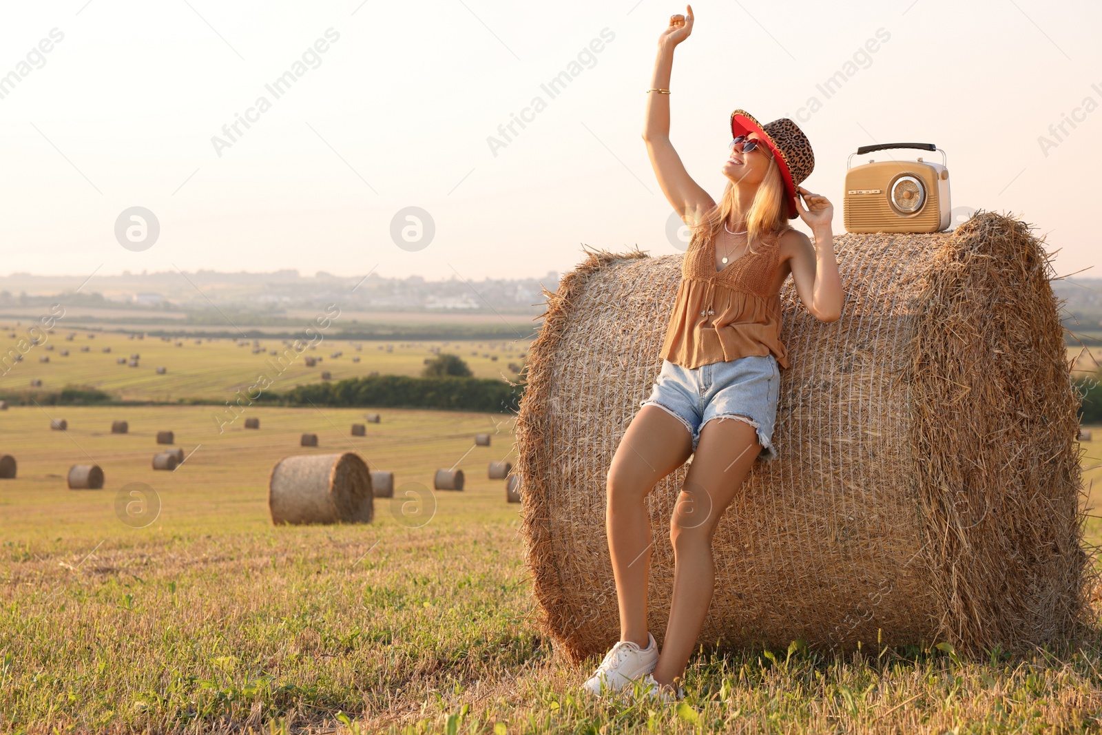 Photo of Happy hippie woman with radio receiver near hay bale in field, space for text