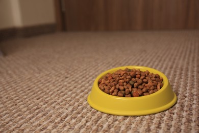 Dry pet food in feeding bowl on soft carpet indoors. Space for text