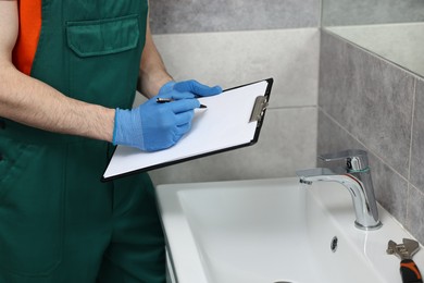 Plumber writing results of examining sink in bathroom, closeup