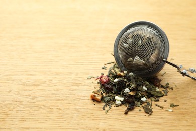 Snap infuser with dried herbal tea leaves on wooden table, closeup. Space for text