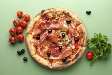 Tasty pizza with cured ham, olives, tomatoes and parsley on green background, top view