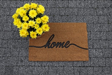 Doormat with word Home and flowers on pavement, flat lay