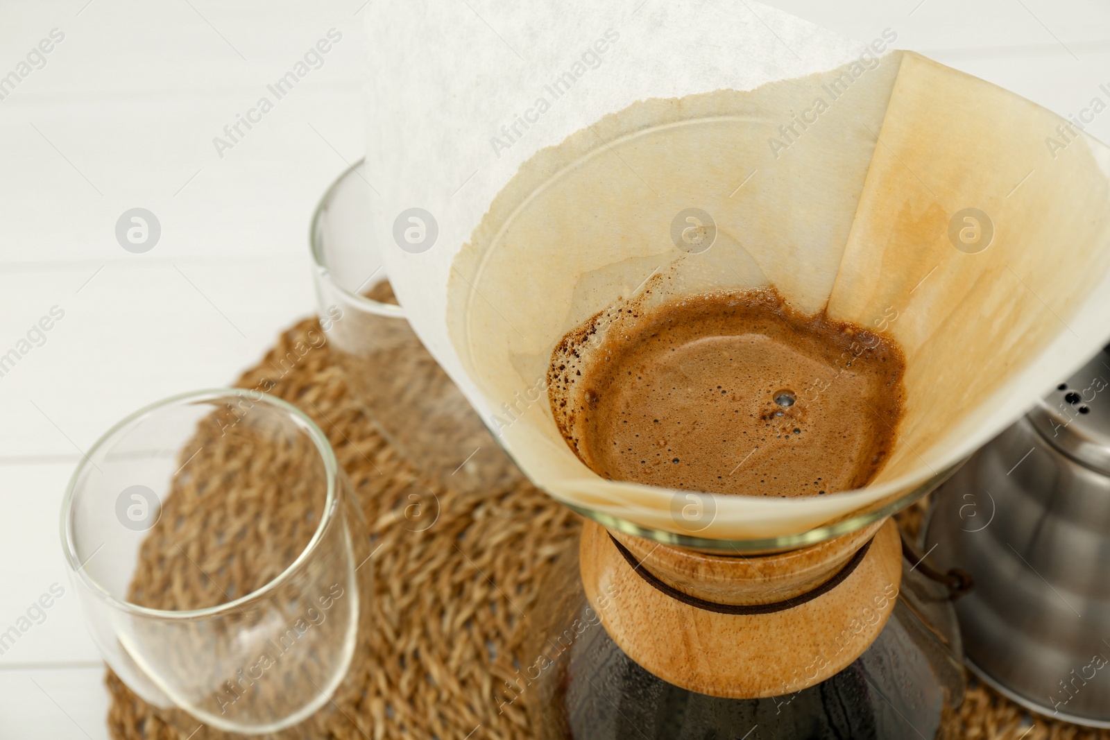 Photo of Paper filter with aromatic drip coffee in glass chemex coffeemaker on table, closeup