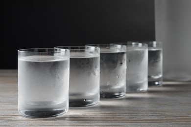 Photo of Shot glasses of cold vodka on wooden table against grey background, closeup