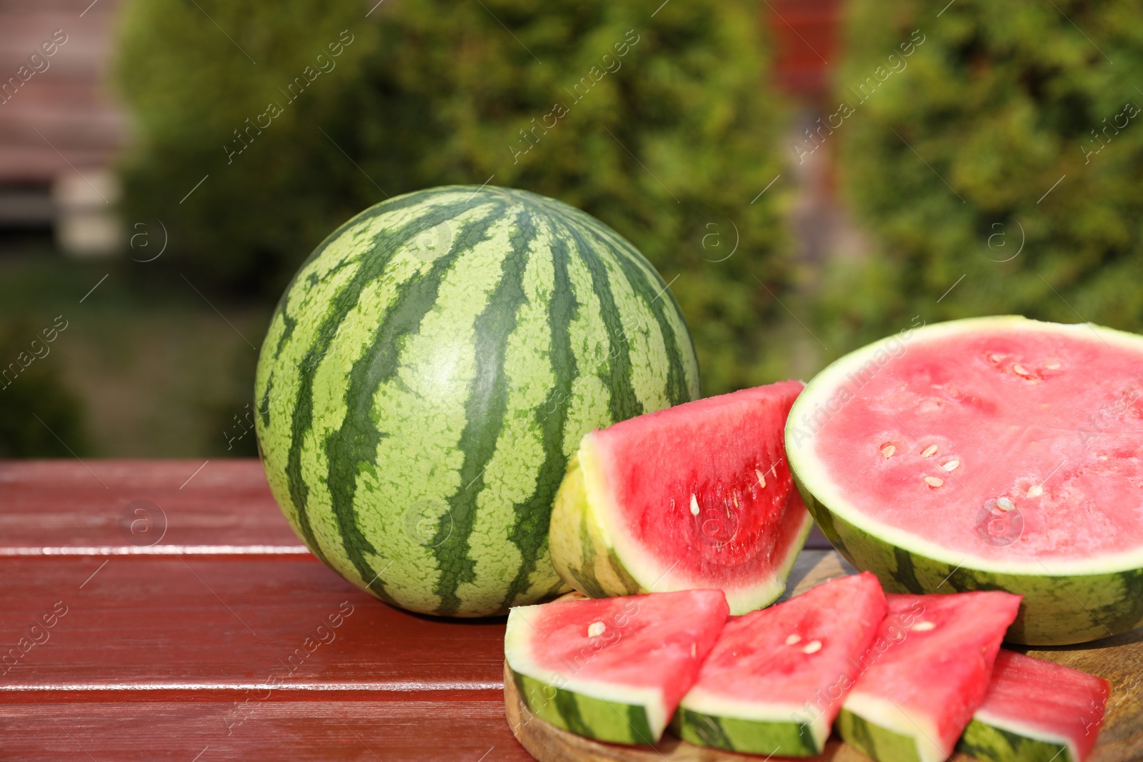 Photo of Delicious cut and whole ripe watermelons on wooden table outdoors