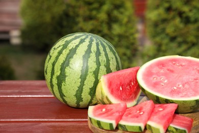 Photo of Delicious cut and whole ripe watermelons on wooden table outdoors