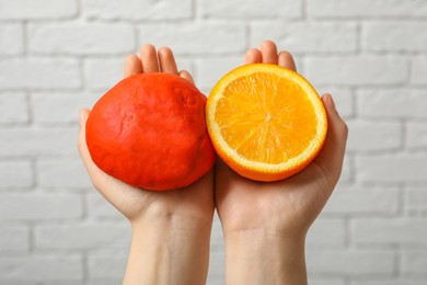 Photo of Woman holding dough painted with natural food coloring and orange near white brick wall, closeup