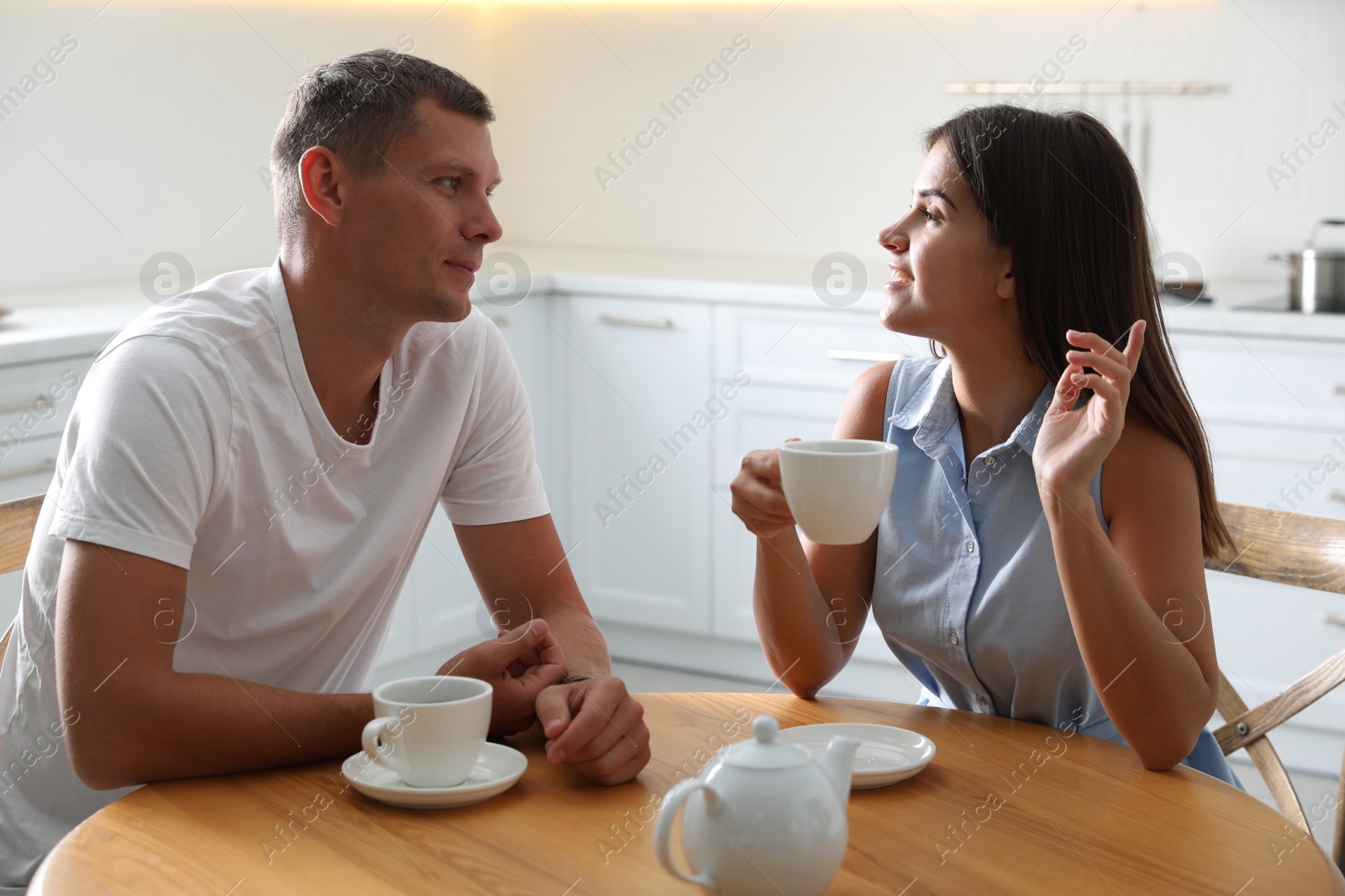 Photo of Man and woman talking while drinking tea at table in kitchen