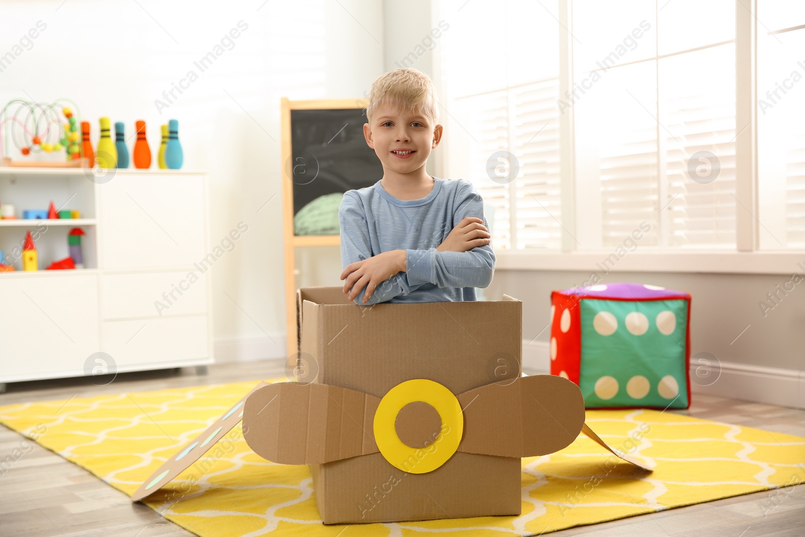 Photo of Little child playing with plane made of cardboard box at home