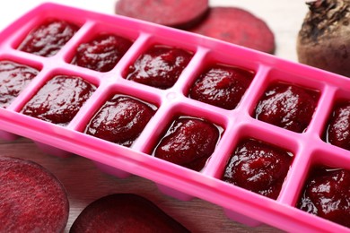 Photo of Beet puree in ice cube tray on table, closeup. Ready for freezing