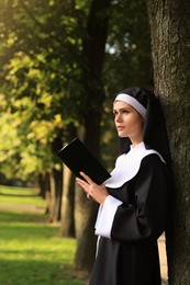 Young nun reading Bible in park on sunny day