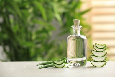 Photo of Bottle with aloe vera juice and slices of fresh leaves on table against blurred background. Space for text