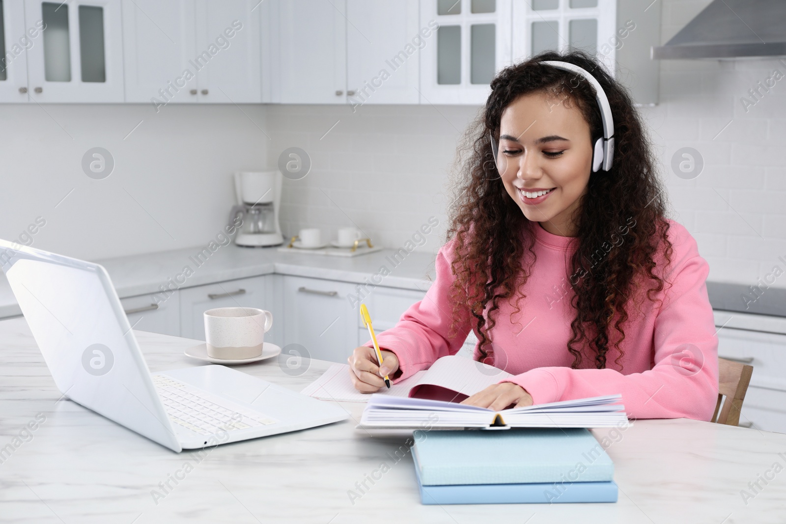 Photo of African American woman with modern laptop and headphones studying in kitchen. Distance learning