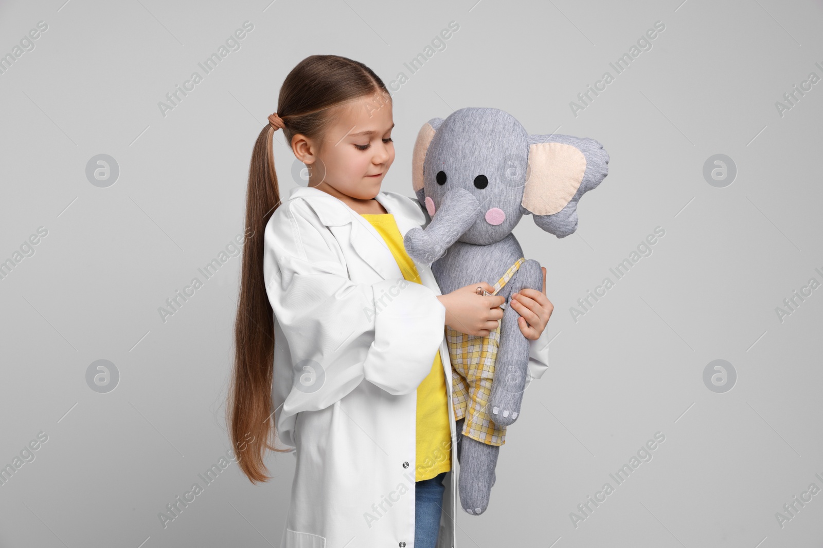 Photo of Little girl playing doctor with toy elephant on light grey background
