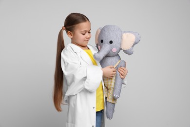 Little girl playing doctor with toy elephant on light grey background