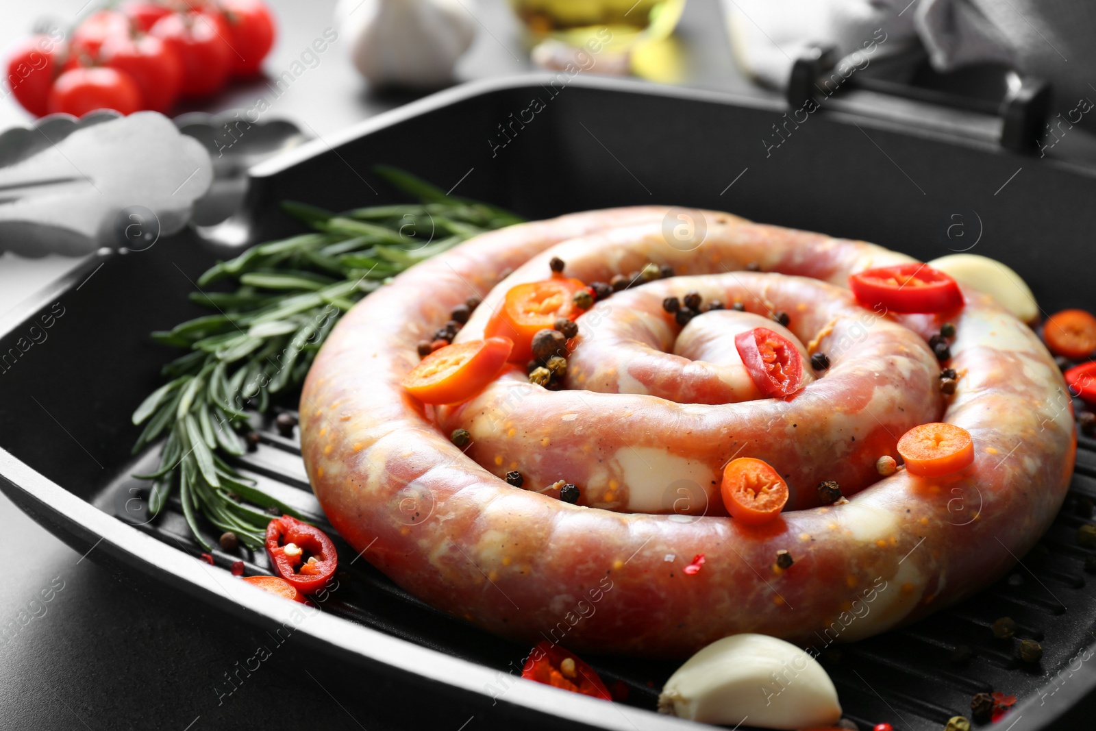 Photo of Pan with raw homemade sausage, chili pepper, garlic and rosemary on grey table, closeup