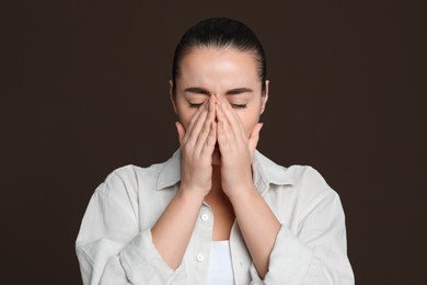 Young woman suffering from headache on dark brown background